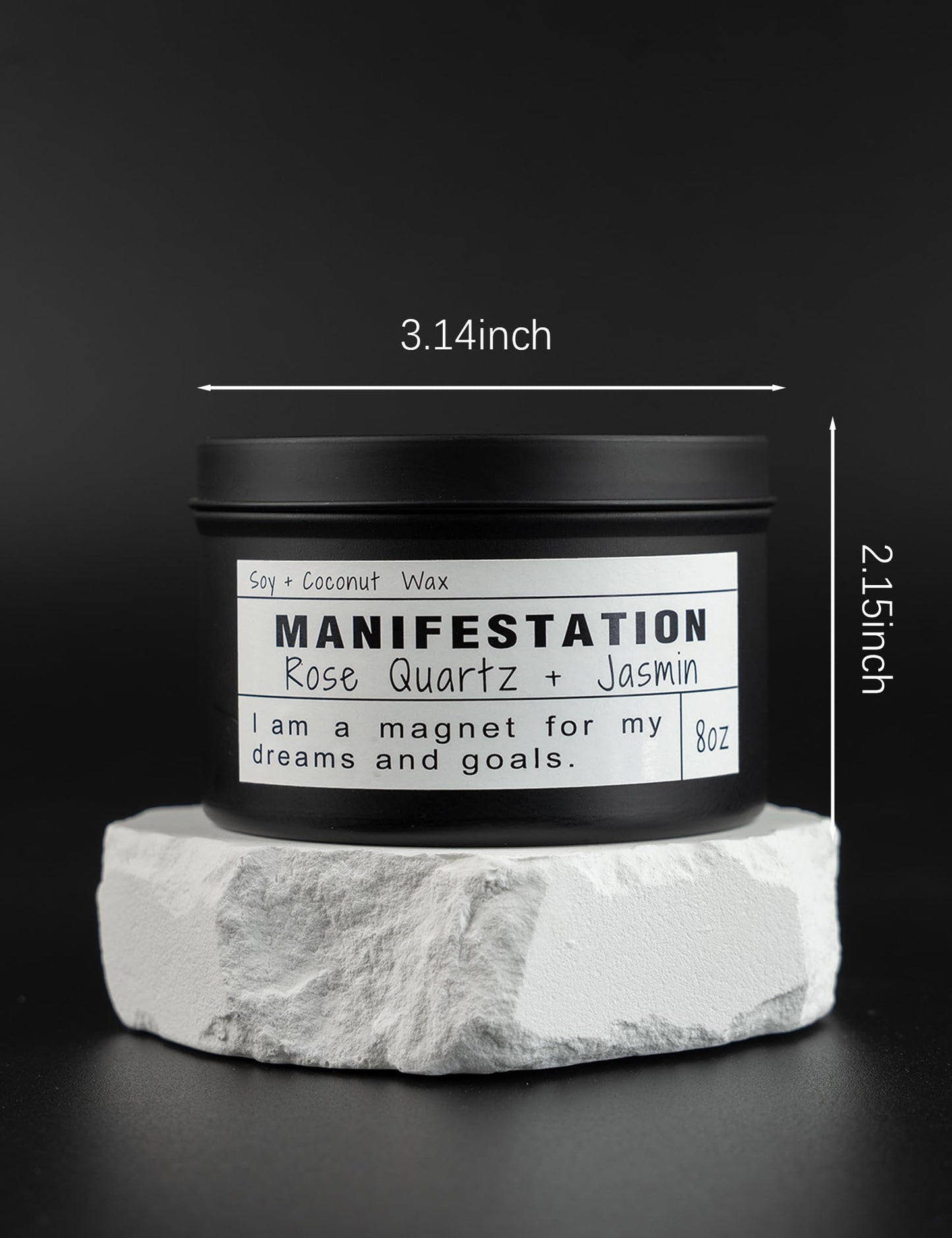 Manifestation candle in a black tin labeled Rose Quartz and Jasmin, shown on a white stone platform with product dimensions 3.14 inches wide and 2.15 inches tall, on a dark background.