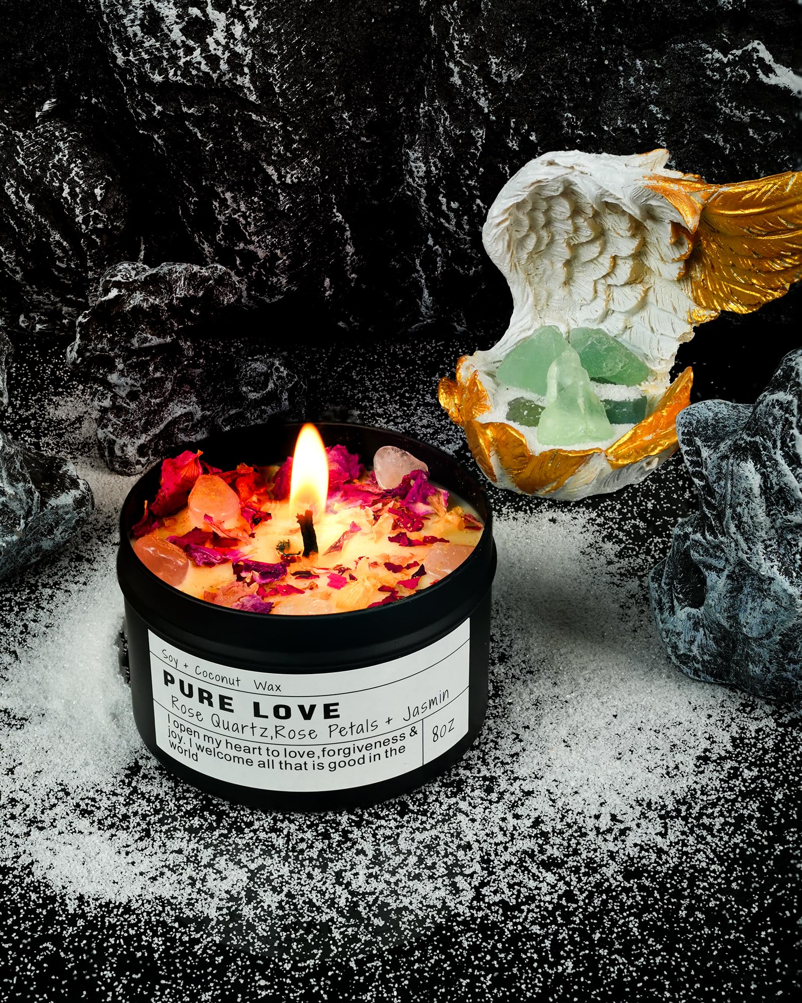 Pure Love candle with rose quartz and petals burning beside an angel figurine and crystals on a dark textured background