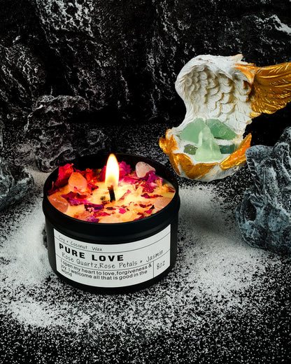 Pure Love candle with rose quartz and petals burning beside an angel figurine and crystals on a dark textured background