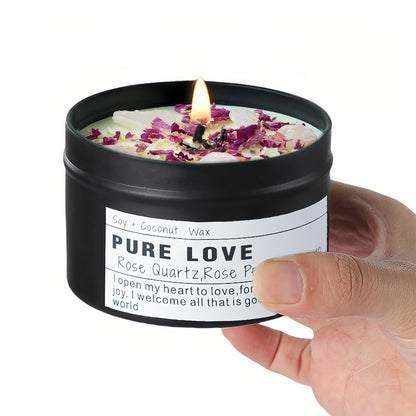 A black tin Pure Love candle topped with rose petals and quartz, held in a hand against a white background.